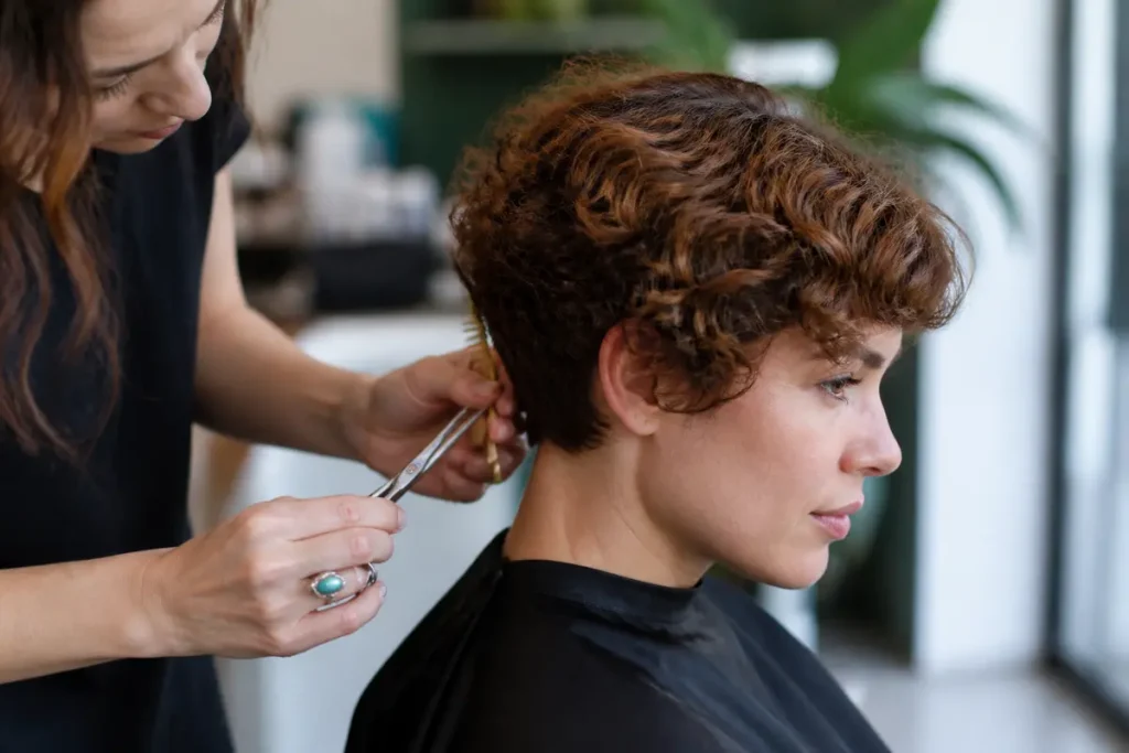 Coiffeuse réalisant un carré court bouclé naturel sur une cliente en salon de coiffure