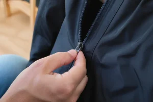Main ajustant une fermeture éclair sur un vêtement sombre, apprendre à réparer une fermeture éclair