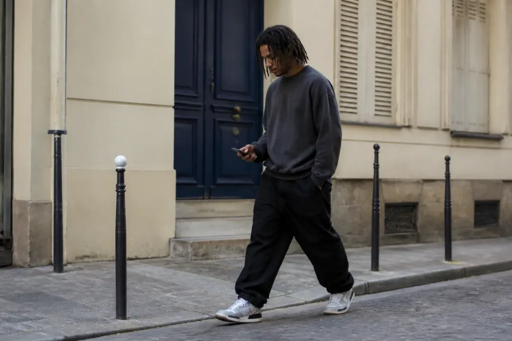 Jeune homme marchant en style streetwear avec un smartphone dans une rue urbaine